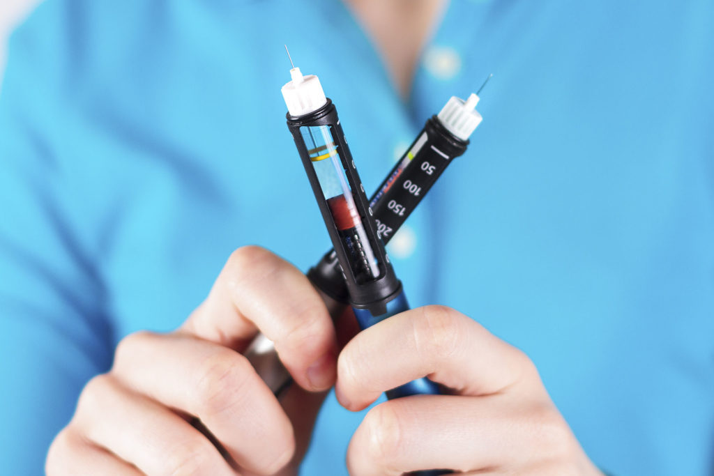 Hand holding insulin pen on white background