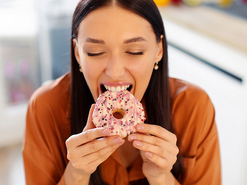A girl with her eyes closed bites a donut
