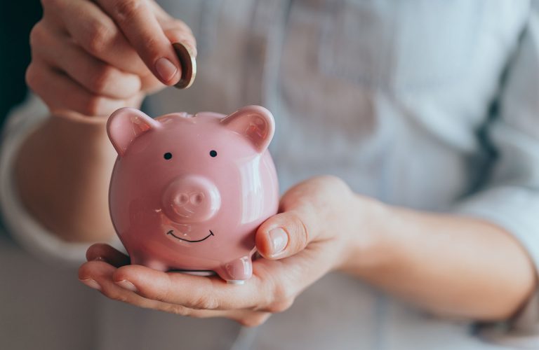 female hands puts a coin in a pink piggy bank. The concept of saving money or savings, investment