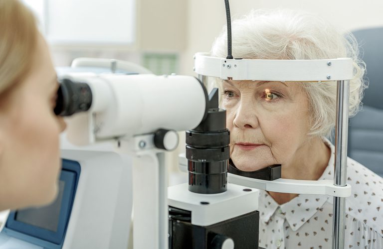 Oculist is sitting afore patient and checking her sight with help of optical equipment