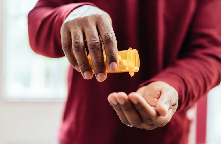 african american man in red shirt pouring pills from prescription pill bottle