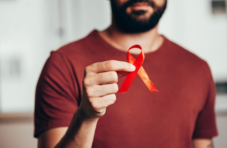 Man holding red ribbon for HIV illness awareness, 1 December World AIDS Day concept.