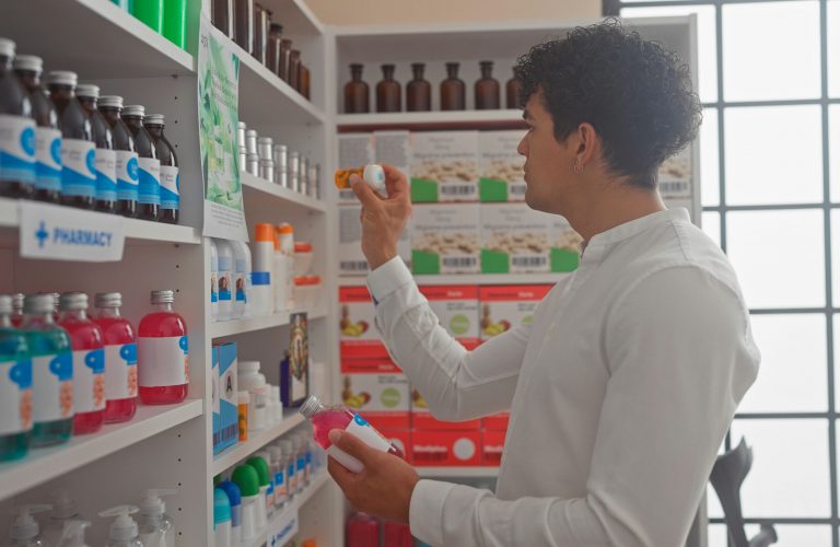 Man comparing drugs at a pharmacy shelf indoors.