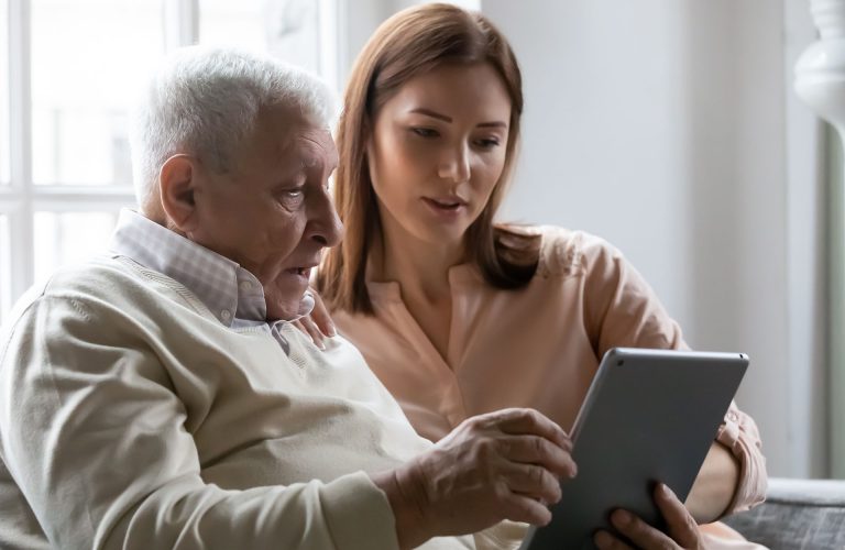 Caring grownup daughter teaching older father to use computer tablet close up, pointing at screen, mature man asking questions about mobile device to young woman, elderly and technology concept
