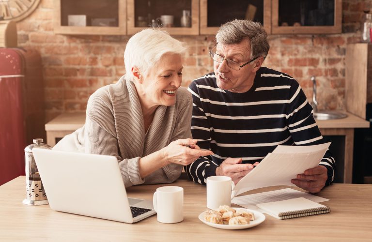 Retirement Financial Planning Concept. Happy Senior Couple Discussing Family Budget Together, Sitting In Kitchen With Laptop And Papers