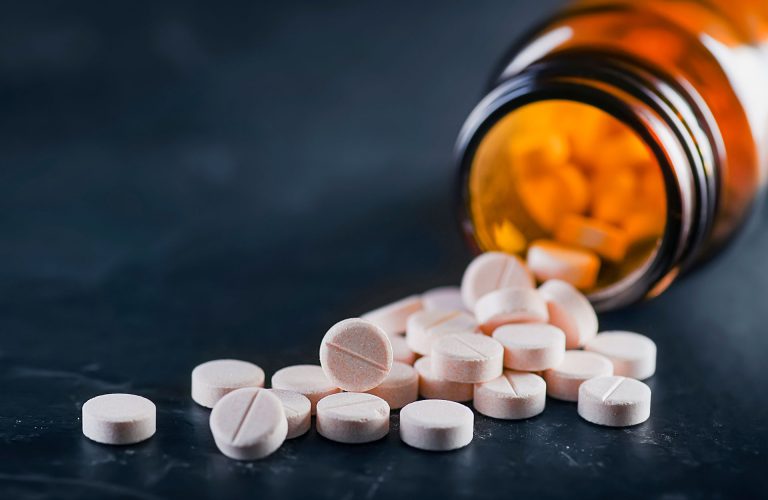 White medical pills or tablets with bottle on black background. Macro side view with copy space.